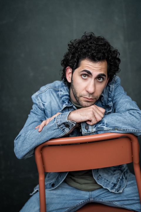 Luca Cundo in a denim jacket, leaning on the back of an orange chair