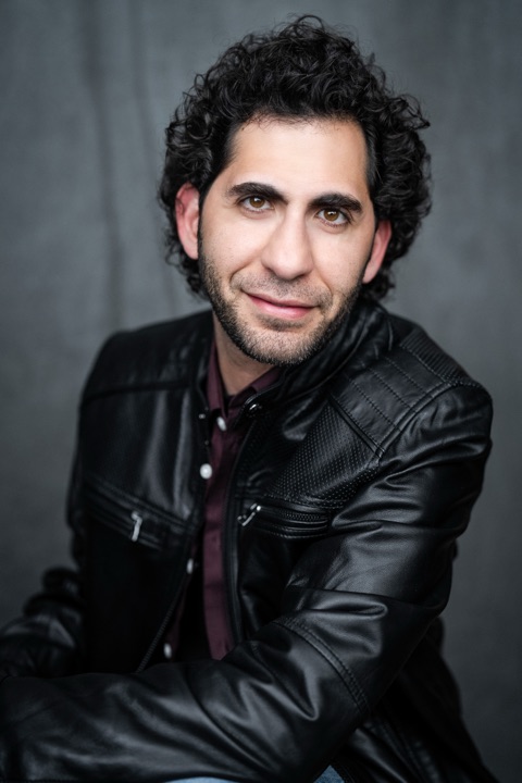 Luca Cundo in a leather jacket with a half smile, grey backdrop