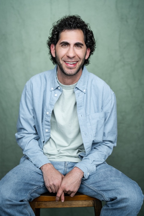 Luca Cundo smiling, seated on a stool in a light blue shirt and jeans